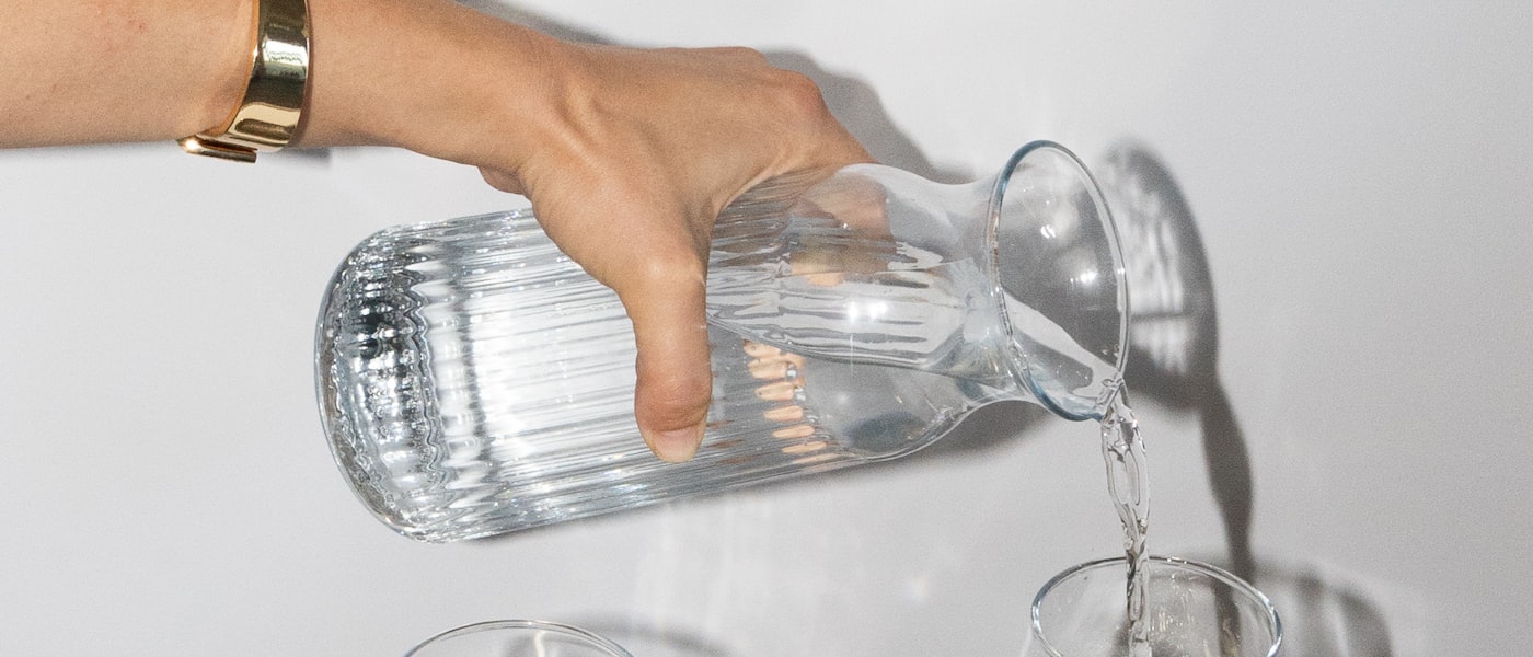 Hand pouring fresh water into a glass — daily hydration